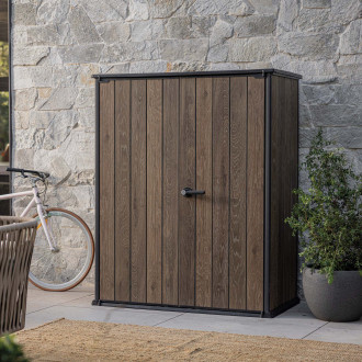 Szafa ogrodowa Deco Vertical 1400L Walnut Keter w drewnianym kolorze ustawiona na tarasie przy kamiennej ścianie