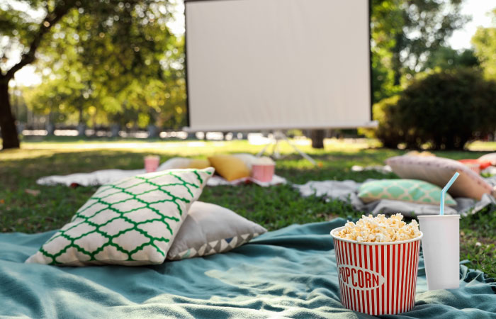 kino plenerowe urządzone w ogrodzie z kolorowymi poduszkami i kocami