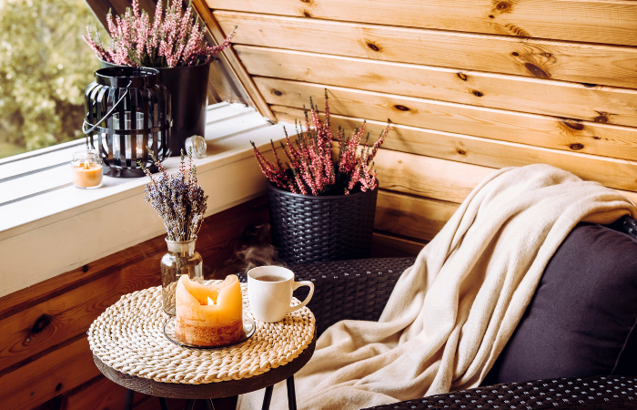 Śliczny hygge wystr&oacute;j tarasu. Kwiaty wrzosu, lawenda w wazonie butelkowym, płomień przy świecach, miękki beżowy kratę czeka na wygodnym fotelu mebli ogrodowych.