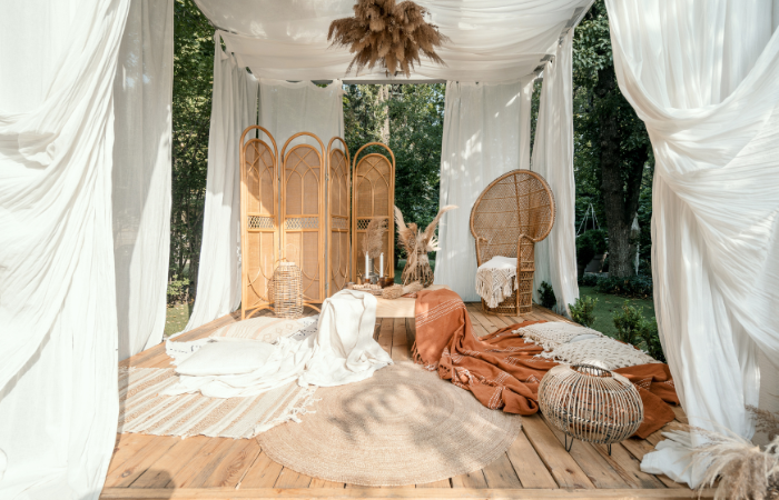 Altanka ogrodowa z rustykalną beżową dekoracją na piknik w ogrodzie, projekt zewnętrzny. Meble wiklinowe na zewnątrz w pergoli boho, nowoczesne podwórko domowe. Letnia altana z naturalną rośliną, drewnianym wystrojem i kocami.