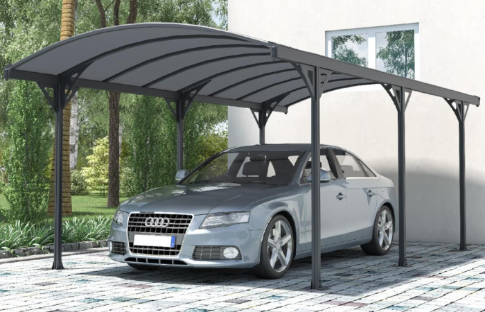 aluminiowa wiata garażowa ustawiona przed domem na kostce brukowej a pod nią wstawiony srebrny samochód audi